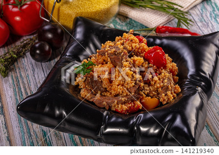 Couscous with tender beef and roasted tomatoes served in black ceramic bowl Couscous with tender beef and roasted tomatoes served in black ceramic bowl 141219340