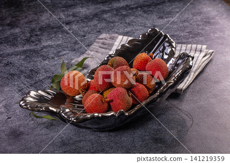 Fresh lychee fruits in black ceramic bowl on dark textured surface 141219359