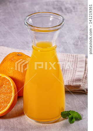 Fresh orange juice in glass carafe with whole and sliced oranges and mint on textured cloth Fresh orange juice in glass carafe with whole and sliced oranges and mint on textured cloth 141219361