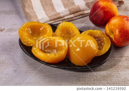 Fresh peach halves on black plate with whole peaches and striped cloth background Fresh peach halves on black plate with whole peaches and striped cloth background 141219392