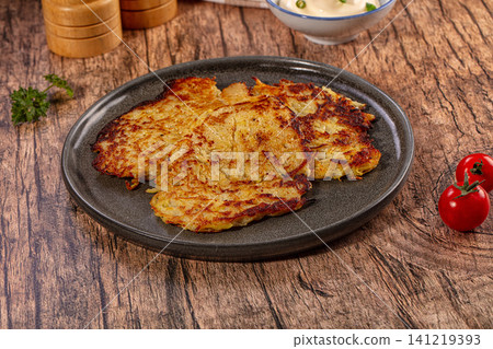 Crispy golden potato pancakes on dark ceramic plate with cherry tomatoes and sour cream Crispy golden potato pancakes on dark ceramic plate with cherry tomatoes and sour cream 141219393