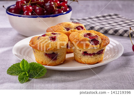 Cherry muffins on white plate with fresh mint and bowl of cherries Cherry muffins on white plate with fresh mint and bowl of cherries 141219396