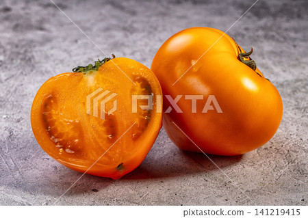 Fresh orange tomato sliced and whole on textured gray surface Fresh orange tomato sliced and whole on textured gray surface 141219415
