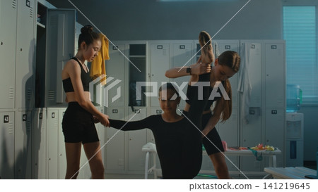 Teen Gymnasts Helping Teammate with Deep Leg Stretch in Locker Room Teen Gymnasts Helping Teammate with Deep Leg Stretch in Locker Room 141219645