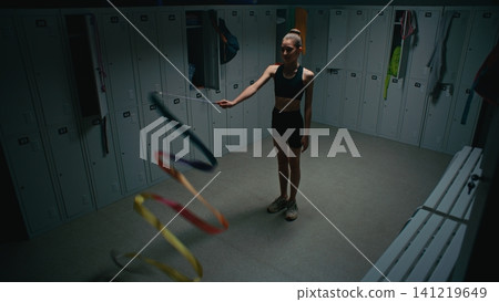 Teen Gymnast Waving Colorful Ribbon in Empty Locker Room Teen Gymnast Waving Colorful Ribbon in Empty Locker Room 141219649