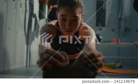 Focused Young Female Athlete Executing Deep Hamstring Stretch on Floor Focused Young Female Athlete Executing Deep Hamstring Stretch on Floor 141219679