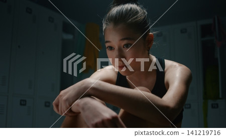 Exhausted Teen Gymnast Hugging Knees in Dark Locker Room Exhausted Teen Gymnast Hugging Knees in Dark Locker Room 141219716