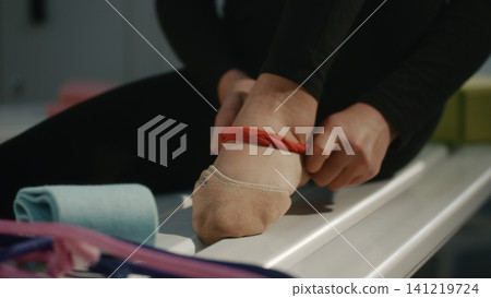 Gymnast Preparing Foot for Training with Elastic Band in Locker Room 141219724