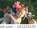 The baby is lying on the grass, surrounded by a pile of stuffed animals 141220197