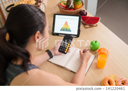 Asian woman using smartphone calculator and notebook for healthy eating meal planning Asian woman using smartphone calculator and notebook for healthy eating meal planning 141220461