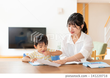 A young boy studying in the living room with his mother. A young boy studying in the living room with his mother. 141220718