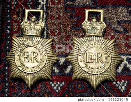 XALO, SPAIN - JUNE 20, 2026.Two brass star shaped badges from the Metropolitan Police are placed together on a patterned oriental rug. The badges show crown details and serve as historical items. XALO, SPAIN - JUNE 20, 2026.Two brass star shaped badges from the Metropolitan Police are placed together on a patterned oriental rug. The badges show crown details and serve as historical items. 141221046