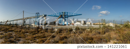The scene shows a large industrial salt production factory in Santa Pola. Blue cranes and conveyor belts are used to process sea salt, with large piles in the background. The scene shows a large industrial salt production factory in Santa Pola. Blue cranes and conveyor belts are used to process sea salt, with large piles in the background. 141221061