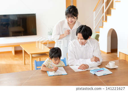 A boy studying at the living room table, watched over by his parents. 141221627