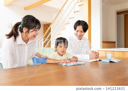 A boy studying at the living room table, watched over by his parents. A boy studying at the living room table, watched over by his parents. 141221631