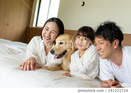 A smiling family of three relaxing on the bed with their beloved dog. A smiling family of three relaxing on the bed with their beloved dog. 141221724