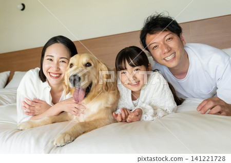 A smiling family of three relaxing on the bed with their beloved dog. A smiling family of three relaxing on the bed with their beloved dog. 141221728