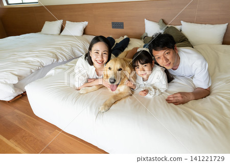 A smiling family of three relaxing on the bed with their beloved dog. A smiling family of three relaxing on the bed with their beloved dog. 141221729