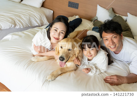一家三口笑容滿面地和他們心愛的狗狗一起躺在床上放鬆。 141221730