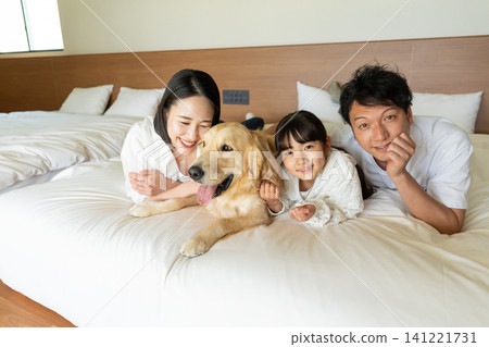 A smiling family of three relaxing on the bed with their beloved dog. A smiling family of three relaxing on the bed with their beloved dog. 141221731