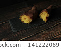 一塊烤得酥脆、熱氣騰騰的紅薯放在木紋桌上，背景是黑色。 141222089