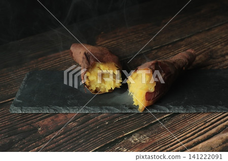 A cracked, steaming roasted sweet potato on a wood-grain table against a black background. A cracked, steaming roasted sweet potato on a wood-grain table against a black background. 141222091