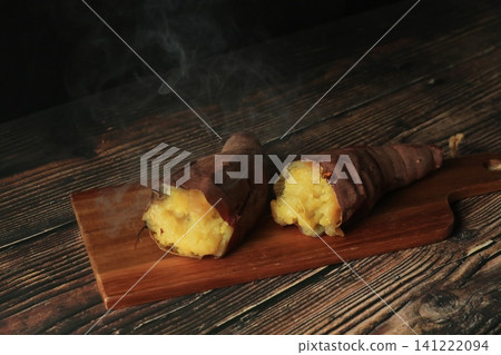 A cracked, steaming roasted sweet potato on a wood-grain table against a black background. A cracked, steaming roasted sweet potato on a wood-grain table against a black background. 141222094