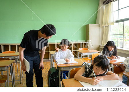 A male teacher smiles and gently instructs elementary school boys studying in the classroom. A male teacher smiles and gently instructs elementary school boys studying in the classroom. 141222624