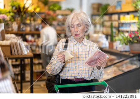 Elderly woman choosing cheese and bacon in grocery supermarket Elderly woman choosing cheese and bacon in grocery supermarket 141222891