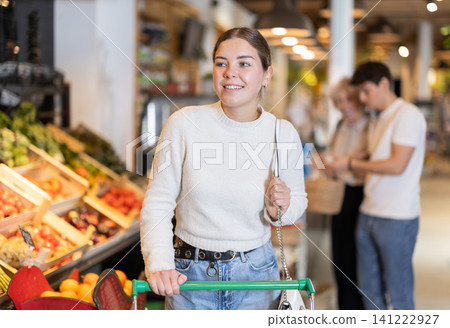 In food store, woman with trolley looking for something on shelf of showcase In food store, woman with trolley looking for something on shelf of showcase 141222927