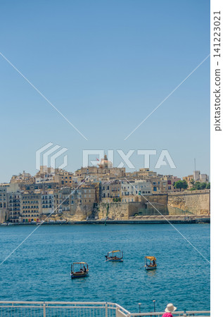 Traditional Maltese dghajsa boats crossing the Grand Harbour with historic limestone fortified town skyline in Malta on a clear summer day. High quality photo Traditional Maltese dghajsa boats crossing the Grand Harbour with historic limestone fortified town skyline in Malta on a clear summer day. High quality photo 141223021