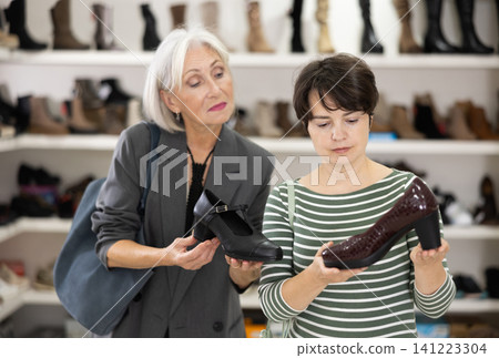 Two women are shopping in shoe store, choose woman dress shoes, classic shoes Two women are shopping in shoe store, choose woman dress shoes, classic shoes 141223304