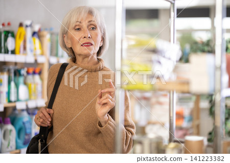 Elderly woman selects various household cleaning products for cleaning house Elderly woman selects various household cleaning products for cleaning house 141223382