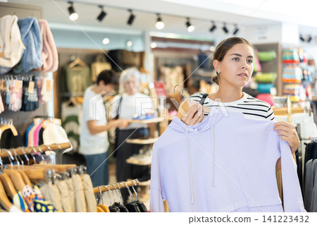 Young girl choosing convenient hoodie in clothing store Young girl choosing convenient hoodie in clothing store 141223432