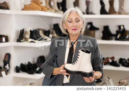 Elderly woman chooses boots in shoe store 141223433