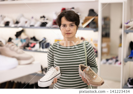 Adult woman chooses sneakers in shoe store Adult woman chooses sneakers in shoe store 141223434