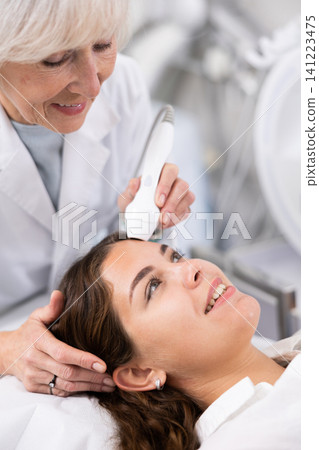 Young woman having face laser therapy procedure by specialist Young woman having face laser therapy procedure by specialist 141223475