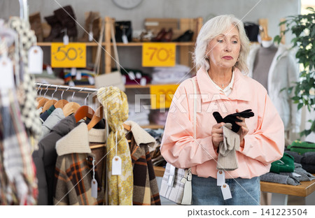Mature woman customer examine and choose gloves in store Mature woman customer examine and choose gloves in store 141223504