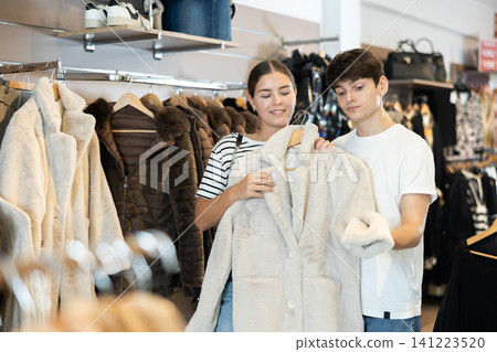 Girl consults with guy male friend about quality fur coat during shopping in clothes store Girl consults with guy male friend about quality fur coat during shopping in clothes store 141223520