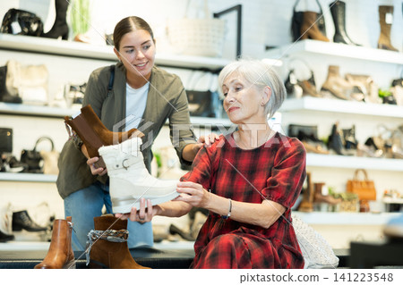 Two female shoppers discussing models of demi-season boots in store Two female shoppers discussing models of demi-season boots in store 141223548
