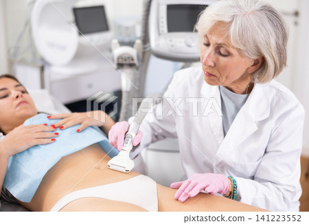 Old woman specialist doing vacuum massage of belly of young woman 141223552
