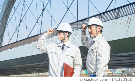 A group of male workers standing in front of a bridge. Infrastructure, construction, building, inspection, bridge, engineer, maintenance, contractor. A group of male workers standing in front of a bridge. Infrastructure, construction, building, inspection, bridge, engineer, maintenance, contractor. 141223598