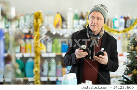 In X mas atmosphere, senior man sniffs fragrance of perfume, chooses scent spray with pleasant smell In X mas atmosphere, senior man sniffs fragrance of perfume, chooses scent spray with pleasant smell 141223600