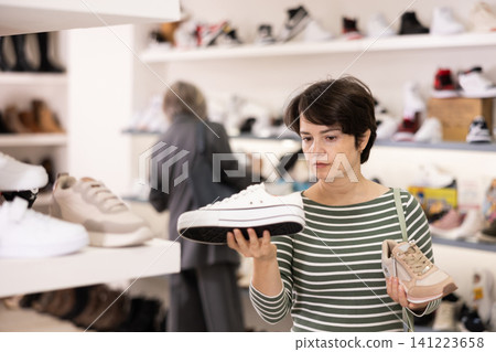 Adult woman chooses sneakers in shoe store Adult woman chooses sneakers in shoe store 141223658