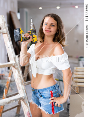 Sexy woman in a white blouse and short shorts poses playfully with a screwdriver in renovated room Sexy woman in a white blouse and short shorts poses playfully with a screwdriver in renovated room 141223660