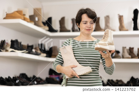 Adult woman chooses high boots in shoe store Adult woman chooses high boots in shoe store 141223702