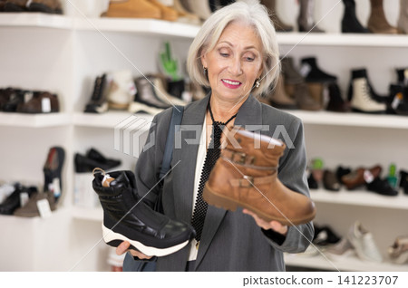 Mature woman takes samples from showcase and examines shoes Mature woman takes samples from showcase and examines shoes 141223707