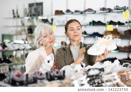 Young colleague shows elderly lady advantages of thick sole in modern sneakers Young colleague shows elderly lady advantages of thick sole in modern sneakers 141223730
