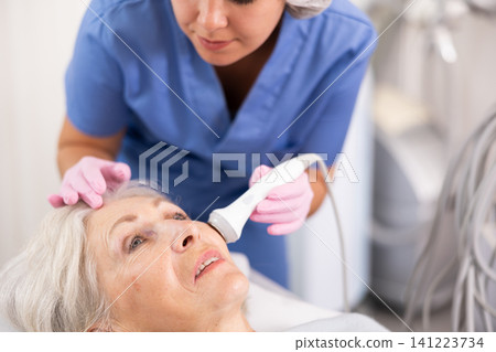 Old woman having face laser therapy procedure Old woman having face laser therapy procedure 141223734
