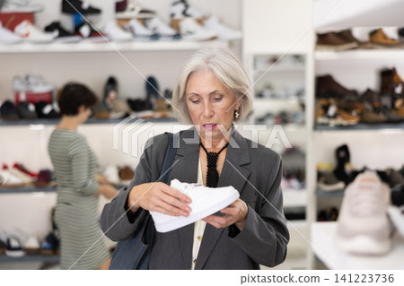 Senior woman takes samples from showcase and examines snickers Senior woman takes samples from showcase and examines snickers 141223736
